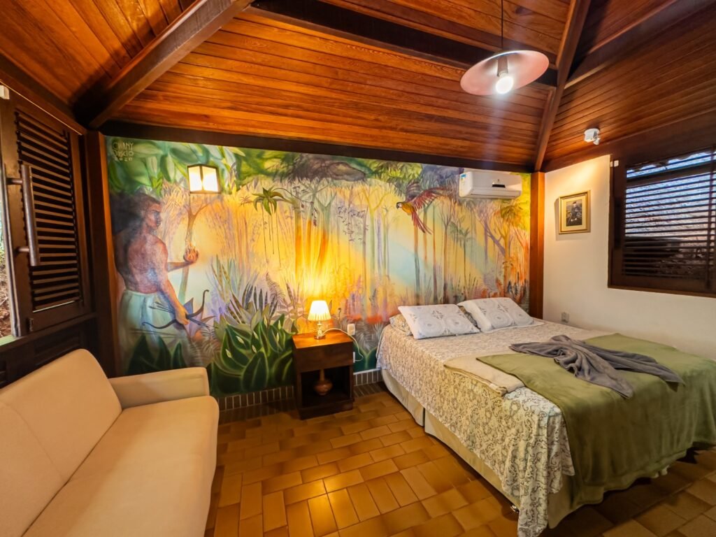 Suíte mobiliada com cama de casal, ar condicionado e sofá, e pintura de quadro na parede de casa de luxo, localizada em Lençóis, na Chapada Diamantina, Bahia